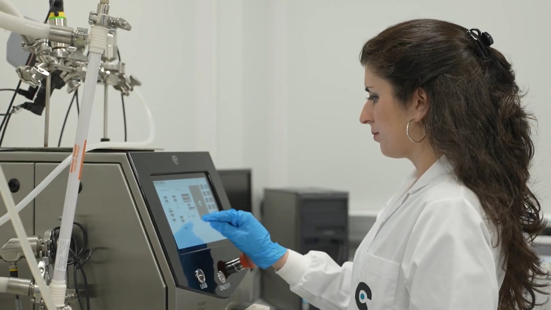 a woman in a white coat touching the touch screen of a bioreactor, is working on a biopharmaceutical application.