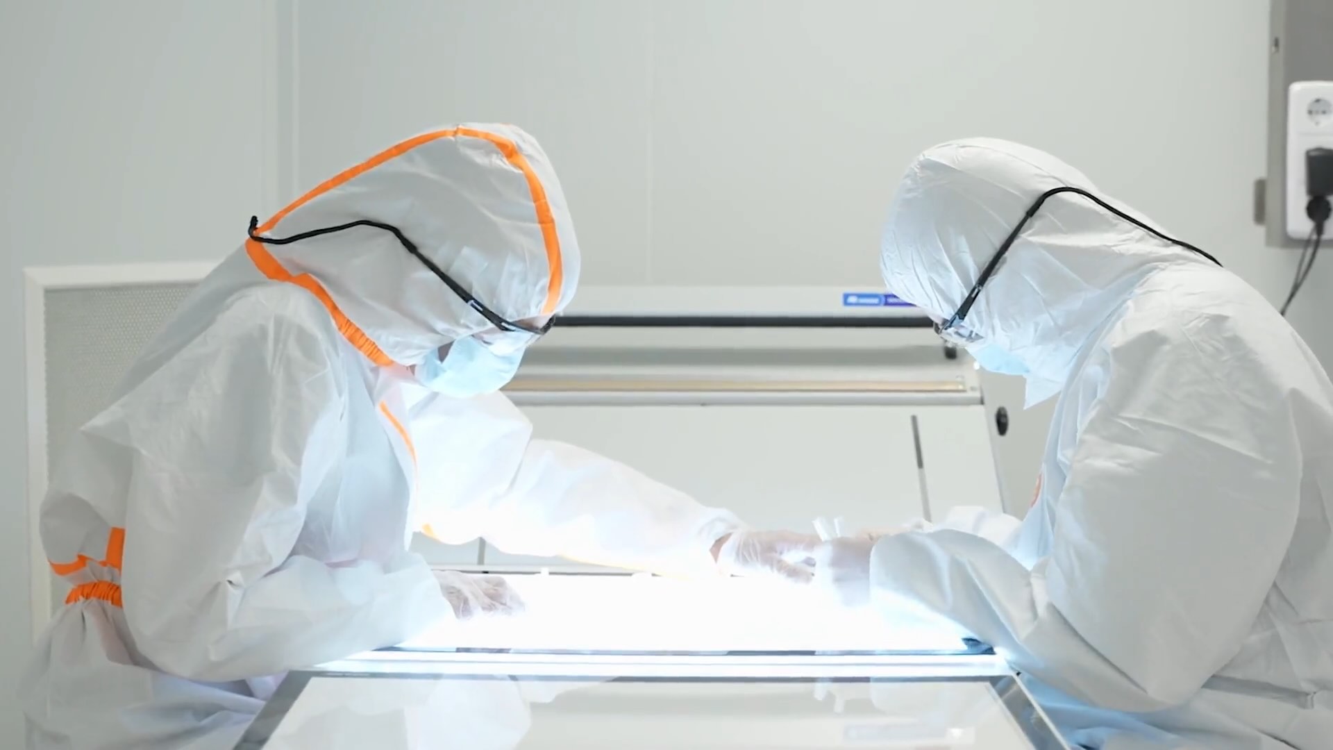 Two people covered entirely in white clothing working in a clean room in a scientific application.