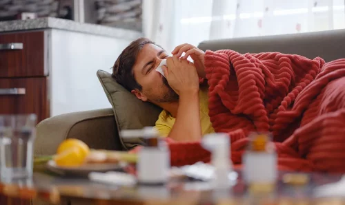 a person stretched out on the couch and covered with a blanket because of a cold