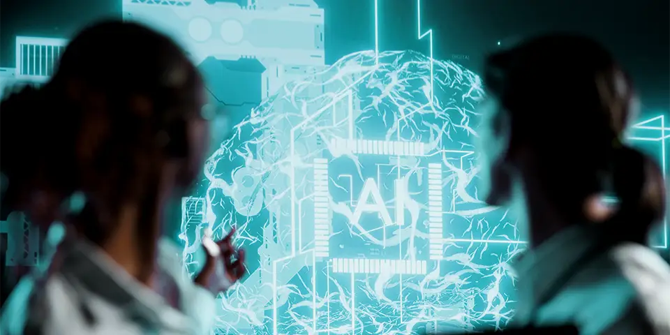 The image shows two scientists or researchers with their backs to the camera. They are looking at a large screen showing a visual representation of a human brain, superimposed with electronic circuits and the word ‘AI’ (artificial intelligence in biopharma).